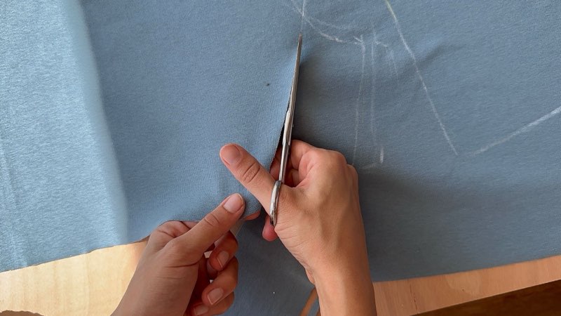 Hands cutting blue cotton jersey along chalk lines